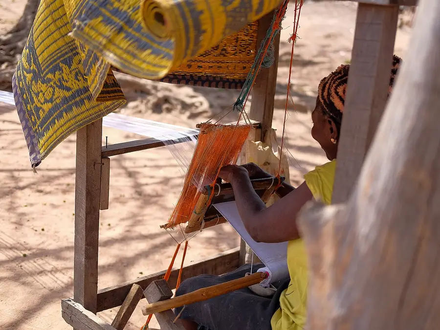Hands working a narrow loom, weaving striped aso-oke cloth.