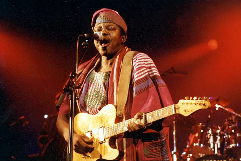 King Sunny Adé on stage in white, playing guitar and singing.
